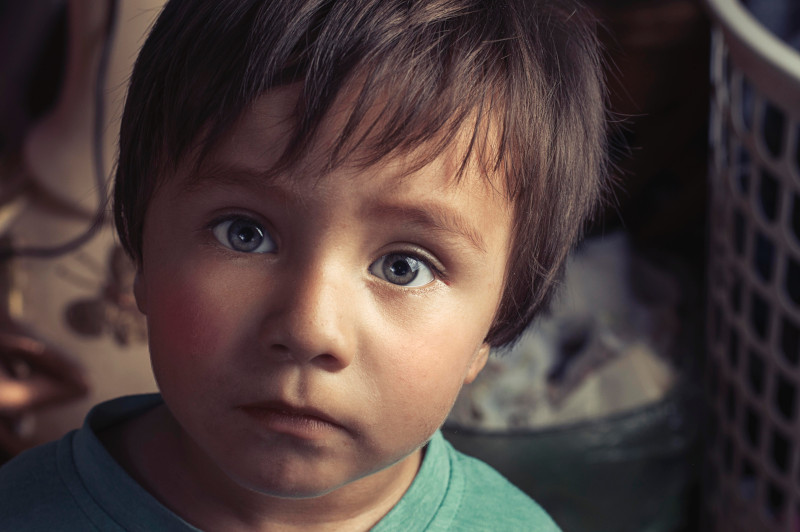Viso di bambino dell'Europa dell'est, dall'espressione profonda, con occhi azzurri e una luce drammatica